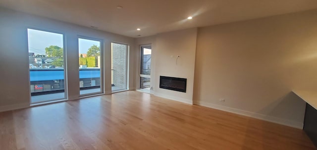 unfurnished living room with a glass covered fireplace, baseboards, light wood-style flooring, and recessed lighting