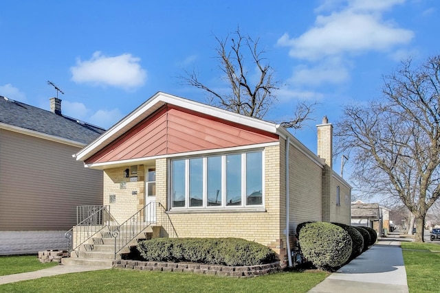 view of front of house with brick siding, a chimney, and a front yard