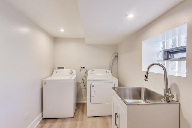 laundry area with light wood finished floors, independent washer and dryer, baseboards, and a sink