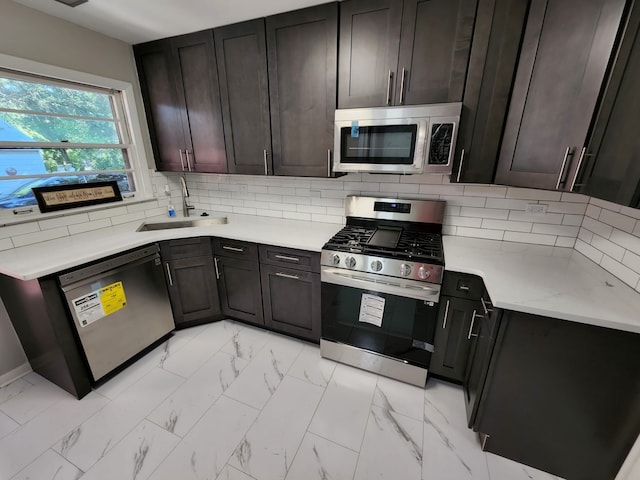 kitchen featuring tasteful backsplash, light countertops, appliances with stainless steel finishes, marble finish floor, and a sink