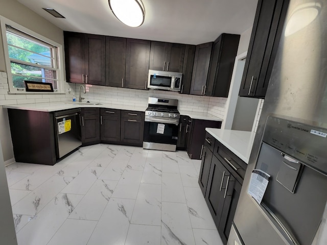 kitchen with tasteful backsplash, light countertops, marble finish floor, stainless steel appliances, and a sink