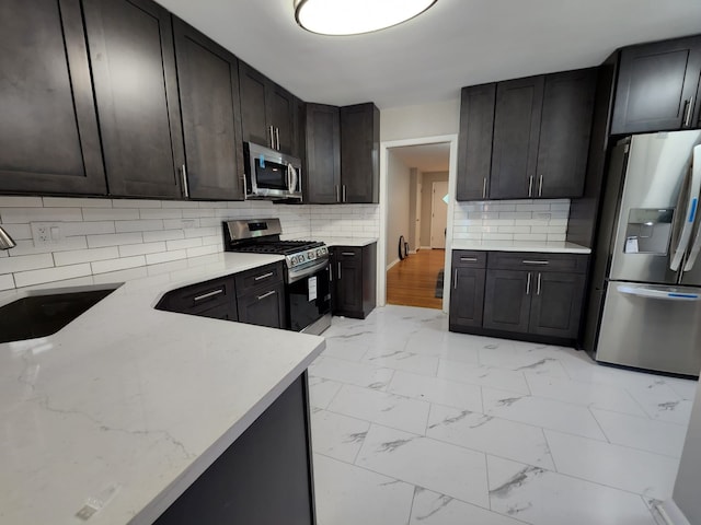 kitchen with tasteful backsplash, light stone counters, marble finish floor, stainless steel appliances, and a sink