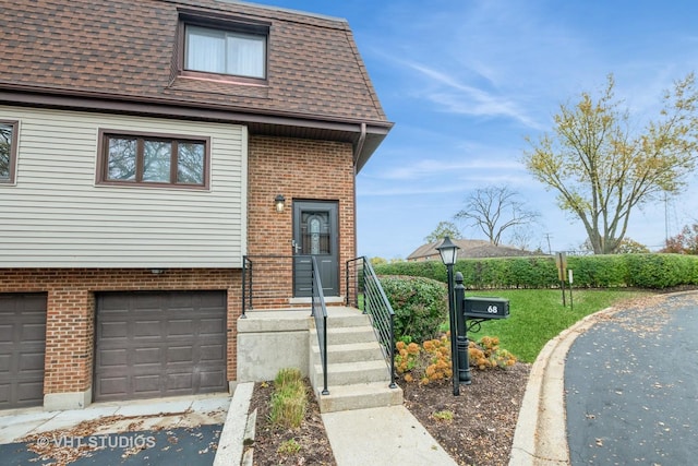 view of front of house featuring an attached garage, brick siding, roof with shingles, and mansard roof