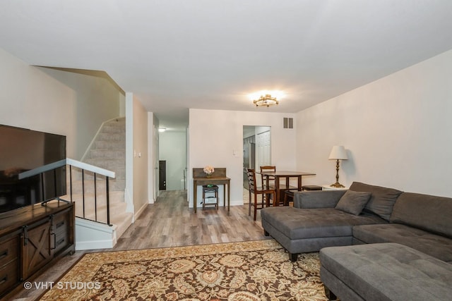 living area with stairs, light wood-style floors, visible vents, and baseboards