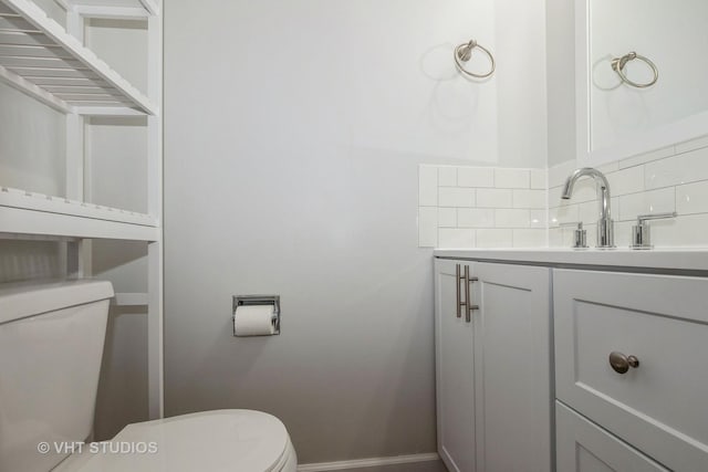 half bathroom featuring decorative backsplash, toilet, vanity, and baseboards