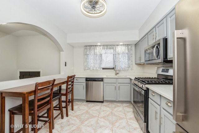 kitchen with a sink, appliances with stainless steel finishes, gray cabinets, and light countertops