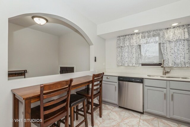 kitchen featuring stainless steel dishwasher, light countertops, a sink, and gray cabinetry