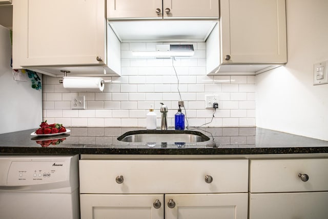 kitchen with backsplash, dark stone counters, white dishwasher, white cabinetry, and a sink