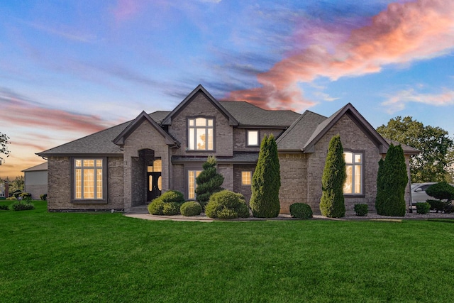 french country inspired facade featuring brick siding, a front lawn, and roof with shingles