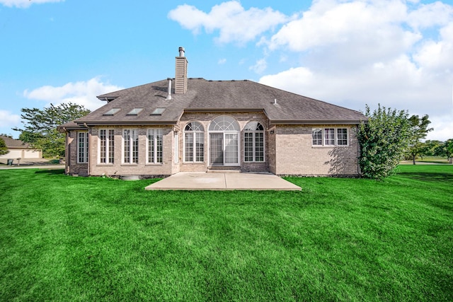 rear view of house featuring a patio, a yard, a shingled roof, brick siding, and a chimney