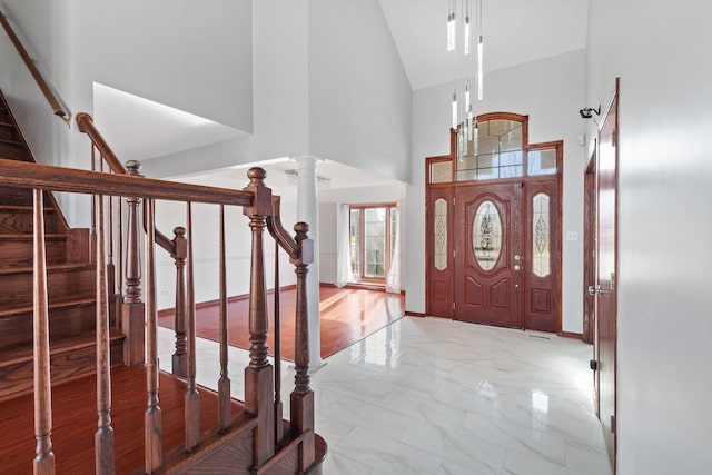 entryway featuring high vaulted ceiling, marble finish floor, stairway, decorative columns, and baseboards