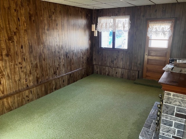 unfurnished dining area featuring a paneled ceiling, wooden walls, a healthy amount of sunlight, and carpet flooring