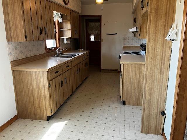 kitchen featuring light floors, baseboards, range with electric cooktop, a sink, and light countertops