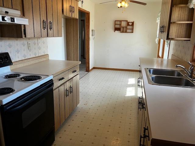 kitchen with black range with electric stovetop, under cabinet range hood, a sink, baseboards, and light floors