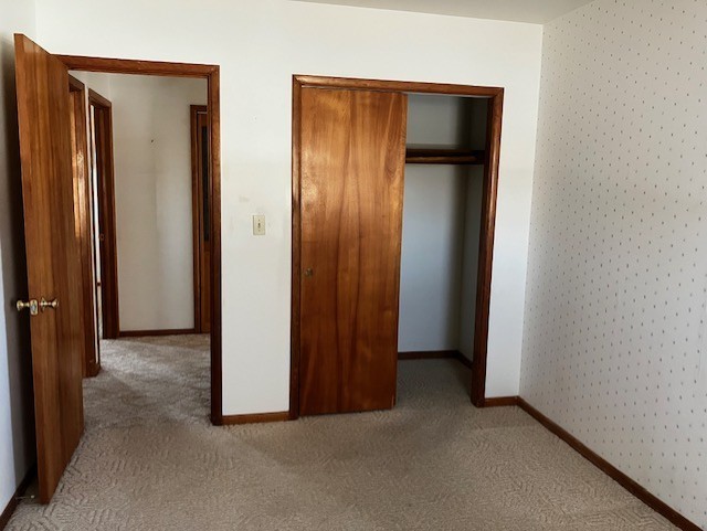 unfurnished bedroom with a closet, baseboards, carpet, and wallpapered walls