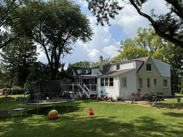 rear view of house featuring a lawn, a chimney, a trampoline, and a sunroom