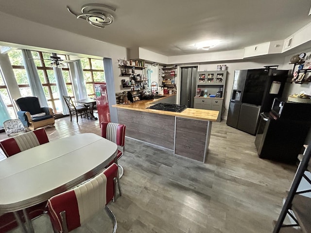 kitchen with a ceiling fan, open shelves, a peninsula, stainless steel fridge with ice dispenser, and black gas stovetop