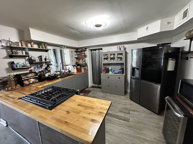 kitchen with fridge with ice dispenser, a sink, open shelves, stovetop, and butcher block counters