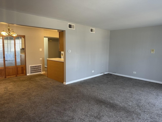 empty room featuring a notable chandelier, visible vents, and dark carpet