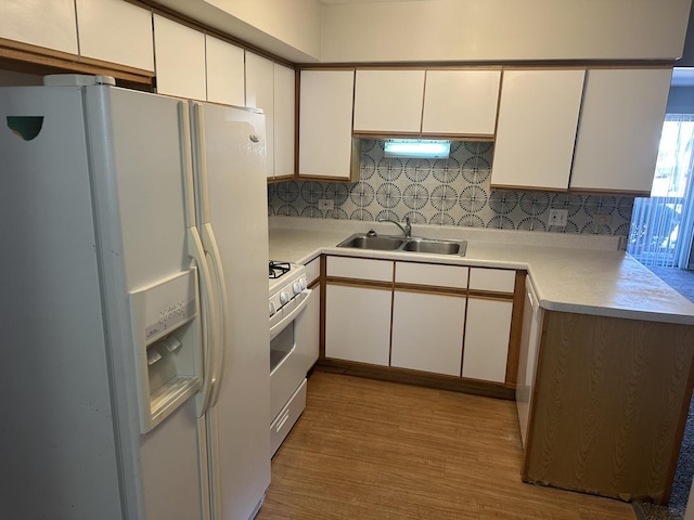 kitchen featuring a sink, white appliances, wood finished floors, and white cabinets