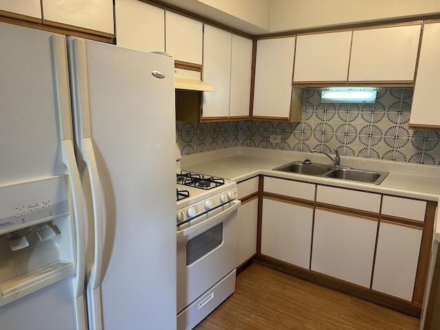 kitchen with white appliances, wood finished floors, a sink, light countertops, and under cabinet range hood