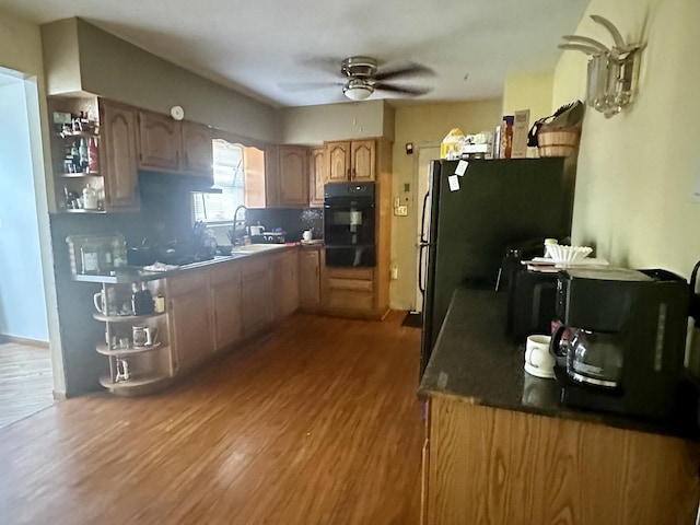 kitchen with a ceiling fan, wood finished floors, freestanding refrigerator, a sink, and dark countertops