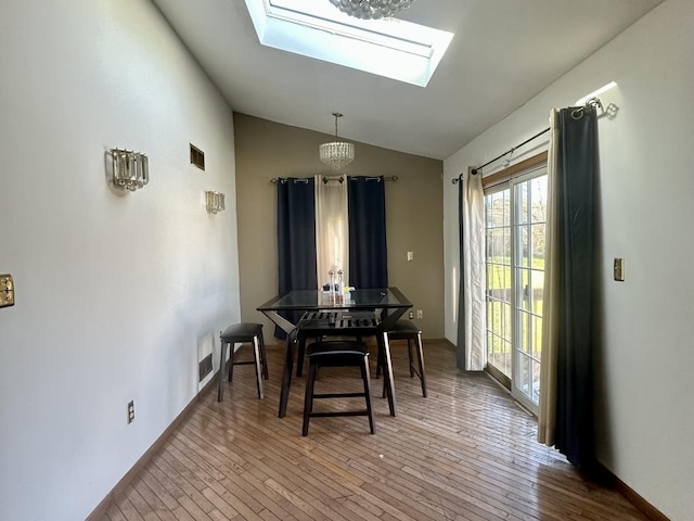 dining space with visible vents, vaulted ceiling with skylight, baseboards, and hardwood / wood-style flooring