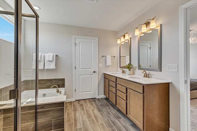 bathroom with double vanity, wood finish floors, a garden tub, and a sink