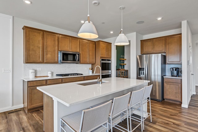 kitchen featuring brown cabinetry, tasteful backsplash, appliances with stainless steel finishes, and a sink