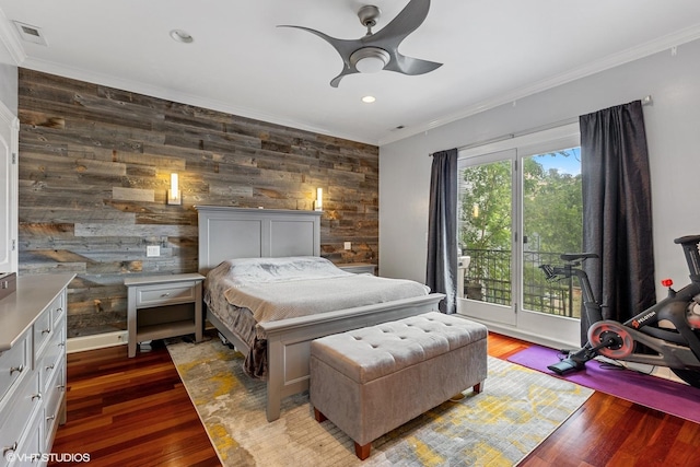 bedroom with an accent wall, wood finished floors, visible vents, and ornamental molding