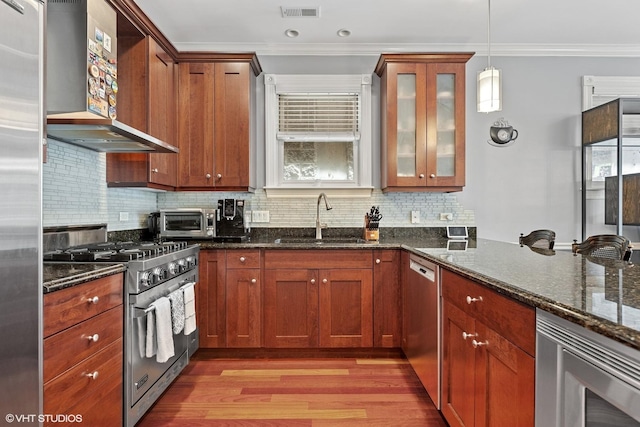 kitchen featuring visible vents, a sink, appliances with stainless steel finishes, crown molding, and wall chimney range hood