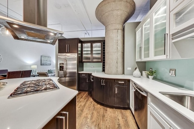 kitchen with island exhaust hood, stainless steel appliances, light countertops, dark brown cabinetry, and light wood-type flooring