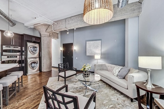 living room featuring stacked washer / dryer, decorative columns, wood finished floors, and a high ceiling