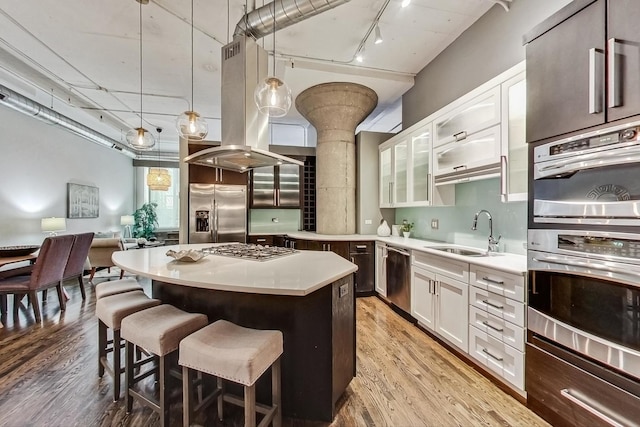 kitchen with light wood-type flooring, a kitchen breakfast bar, island exhaust hood, stainless steel appliances, and a sink