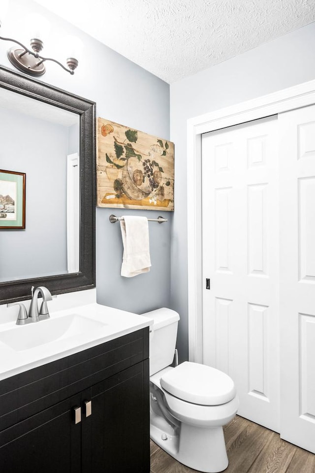 half bathroom with vanity, toilet, wood finished floors, and a textured ceiling