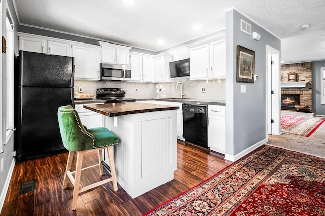 kitchen with dark countertops, visible vents, white cabinets, black appliances, and a sink