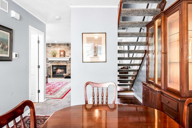 dining room with visible vents, a fireplace, stairs, a textured ceiling, and carpet flooring