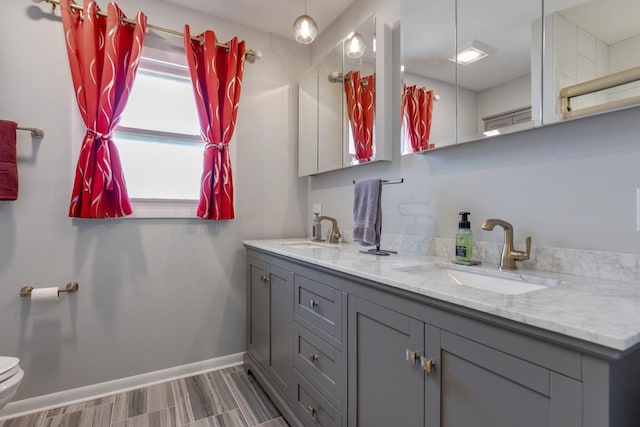 bathroom with double vanity, toilet, baseboards, and a sink