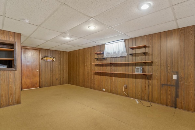 below grade area featuring a drop ceiling, carpet, and wood walls