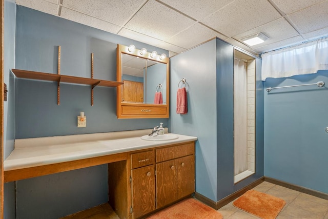 full bathroom featuring a shower, a drop ceiling, baseboards, and vanity