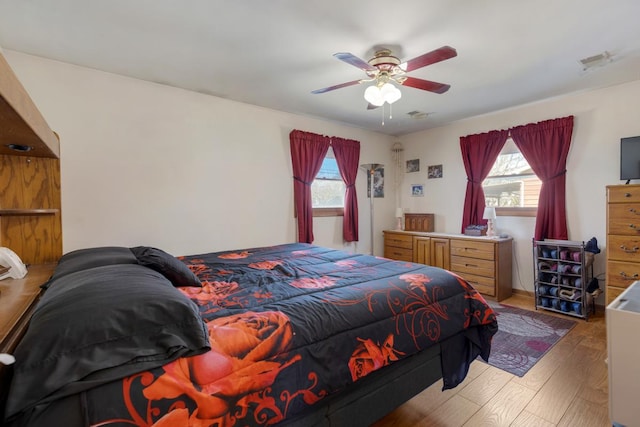 bedroom with ceiling fan, visible vents, multiple windows, and wood finished floors