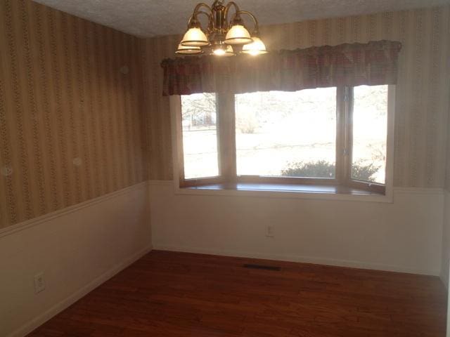 spare room with wallpapered walls, baseboards, wood finished floors, a notable chandelier, and a textured ceiling