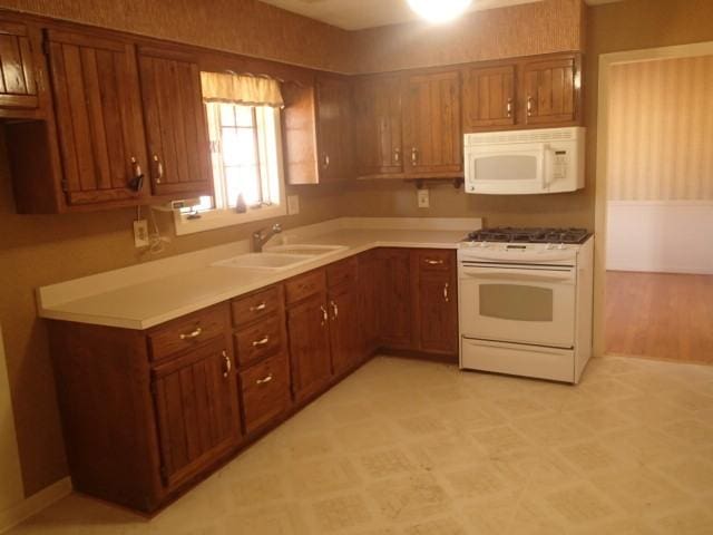 kitchen featuring brown cabinets, a sink, white appliances, light countertops, and light floors