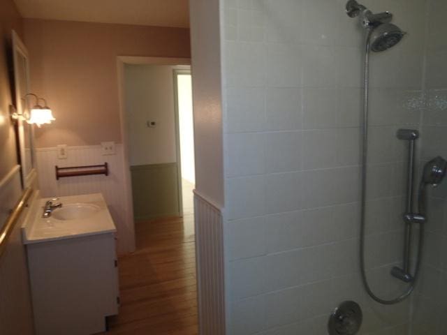 full bath with wainscoting, tiled shower, vanity, and wood finished floors