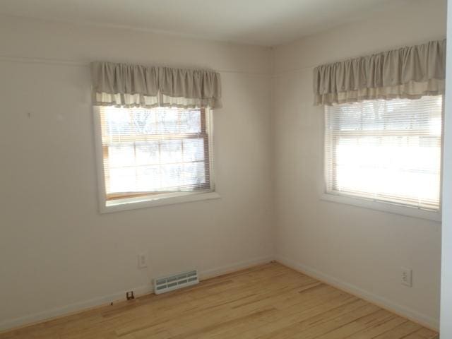 empty room featuring a wealth of natural light, visible vents, light wood-type flooring, and baseboards