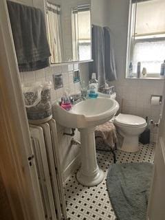 bathroom featuring tile patterned flooring, radiator, toilet, and tile walls