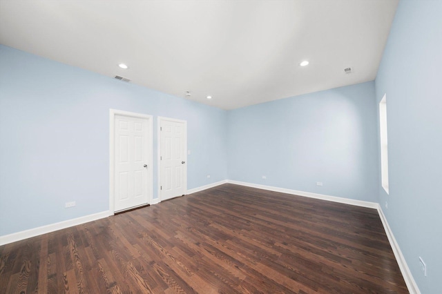 empty room with dark wood-style floors, visible vents, and baseboards