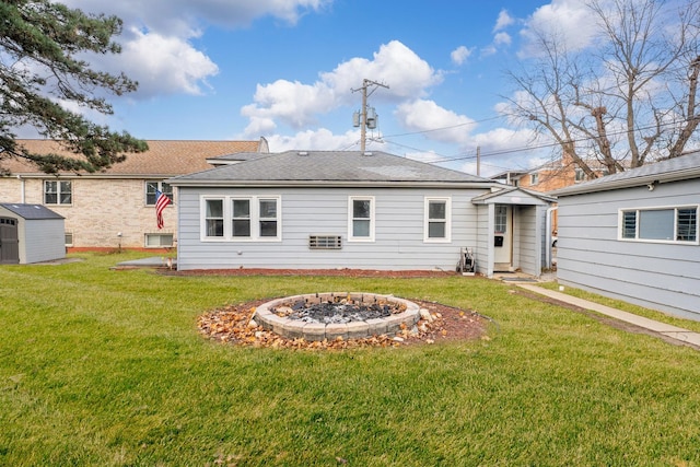 rear view of property featuring a fire pit, a shed, roof with shingles, a lawn, and an outbuilding