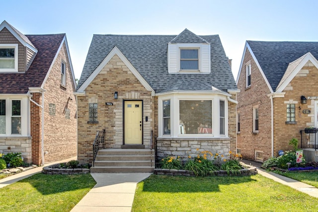 view of front facade with stone siding, roof with shingles, and a front lawn