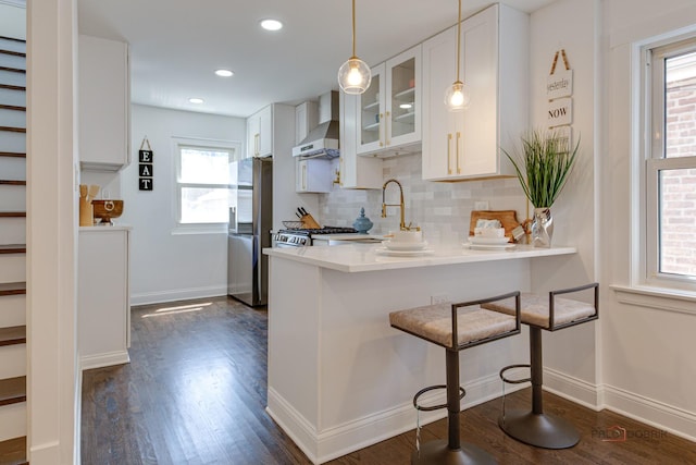 kitchen with tasteful backsplash, dark wood finished floors, a kitchen breakfast bar, freestanding refrigerator, and wall chimney exhaust hood